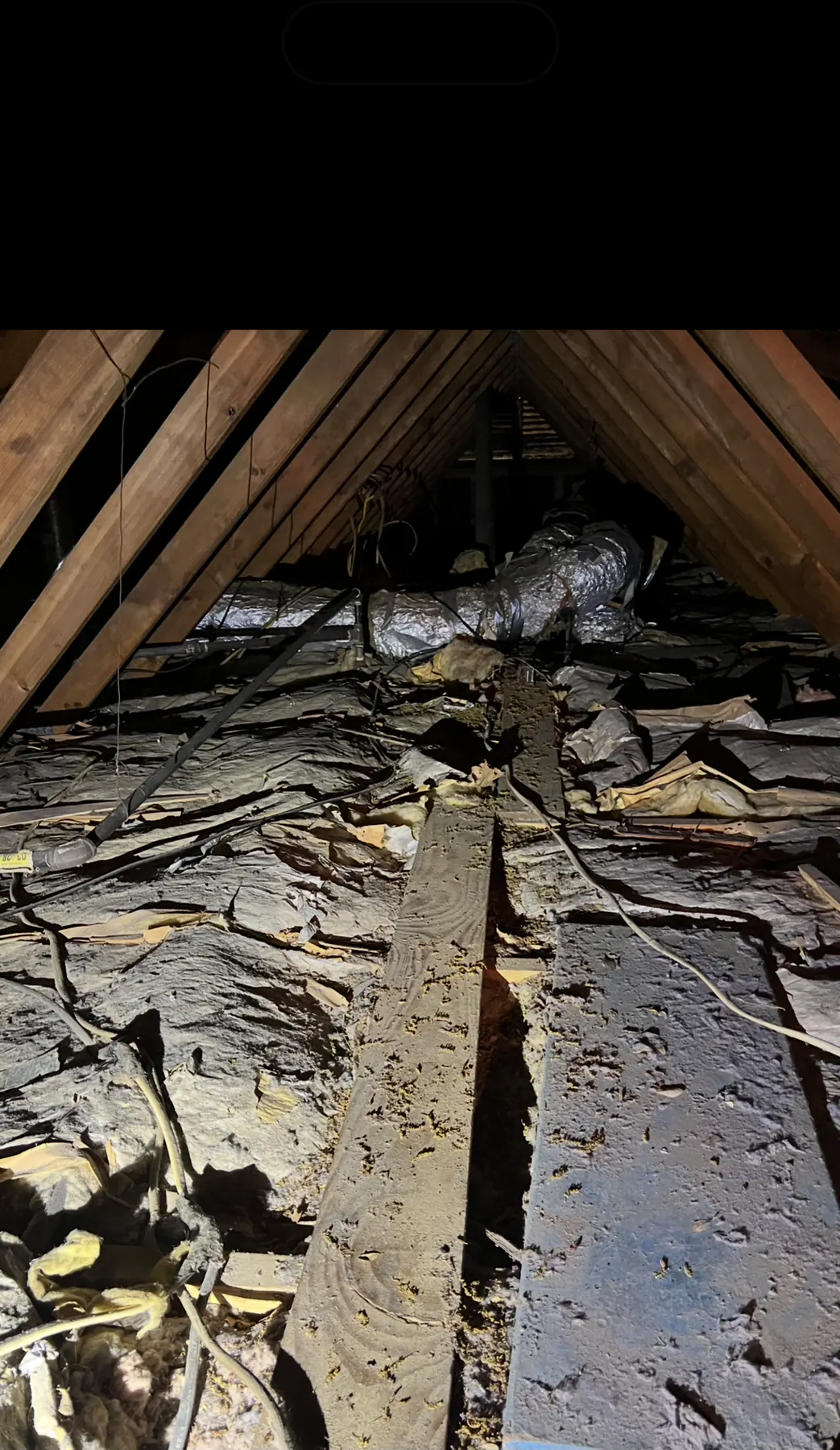 Residential attic with disturbed insulation and exposed framing before restoration